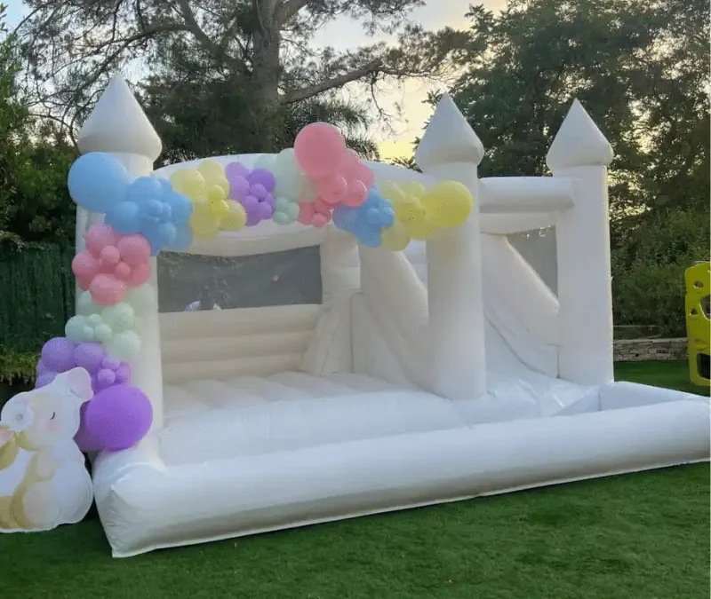vue de biais dans un jardin de la location de château gonflable blanc avec des ballons